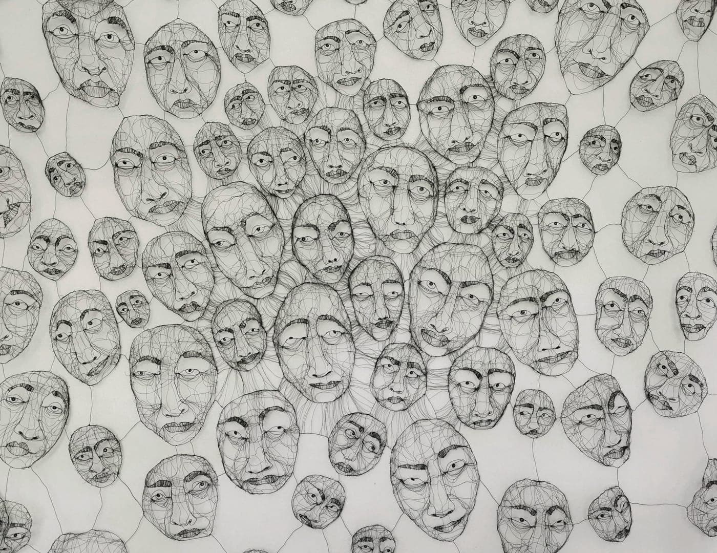 Un mur de rostres de filferro de Fiona Morley, desenes d'ells units per fins fils de filferro, cadascun amb la seva pròpia expressió