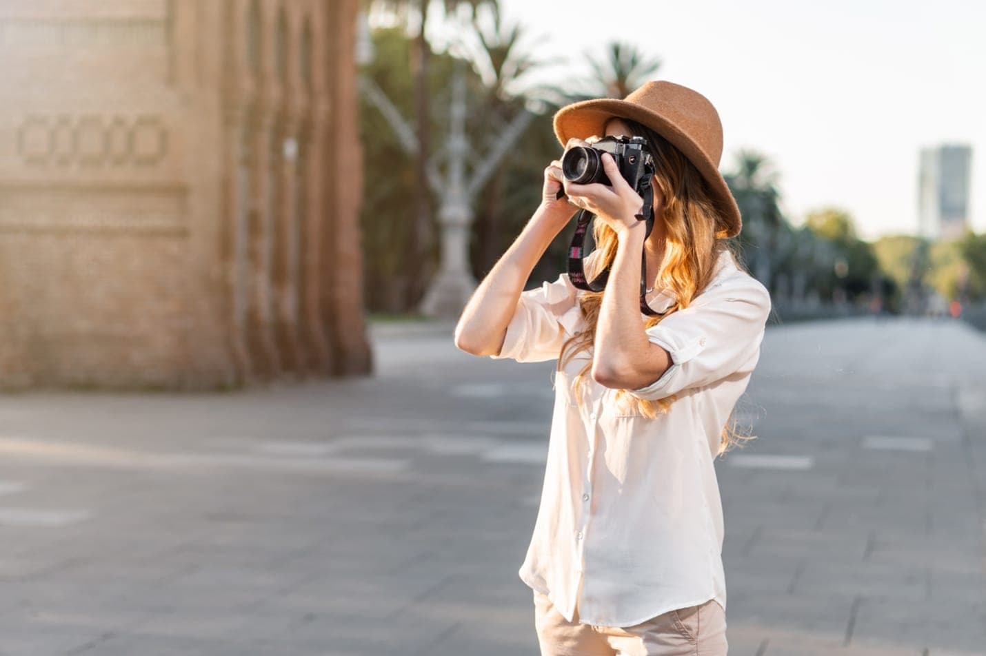 Eine Fotografin mit Kamera und breitkrempigem Hut fotografiert bei Sonnenuntergang eine Straße in Barcelona